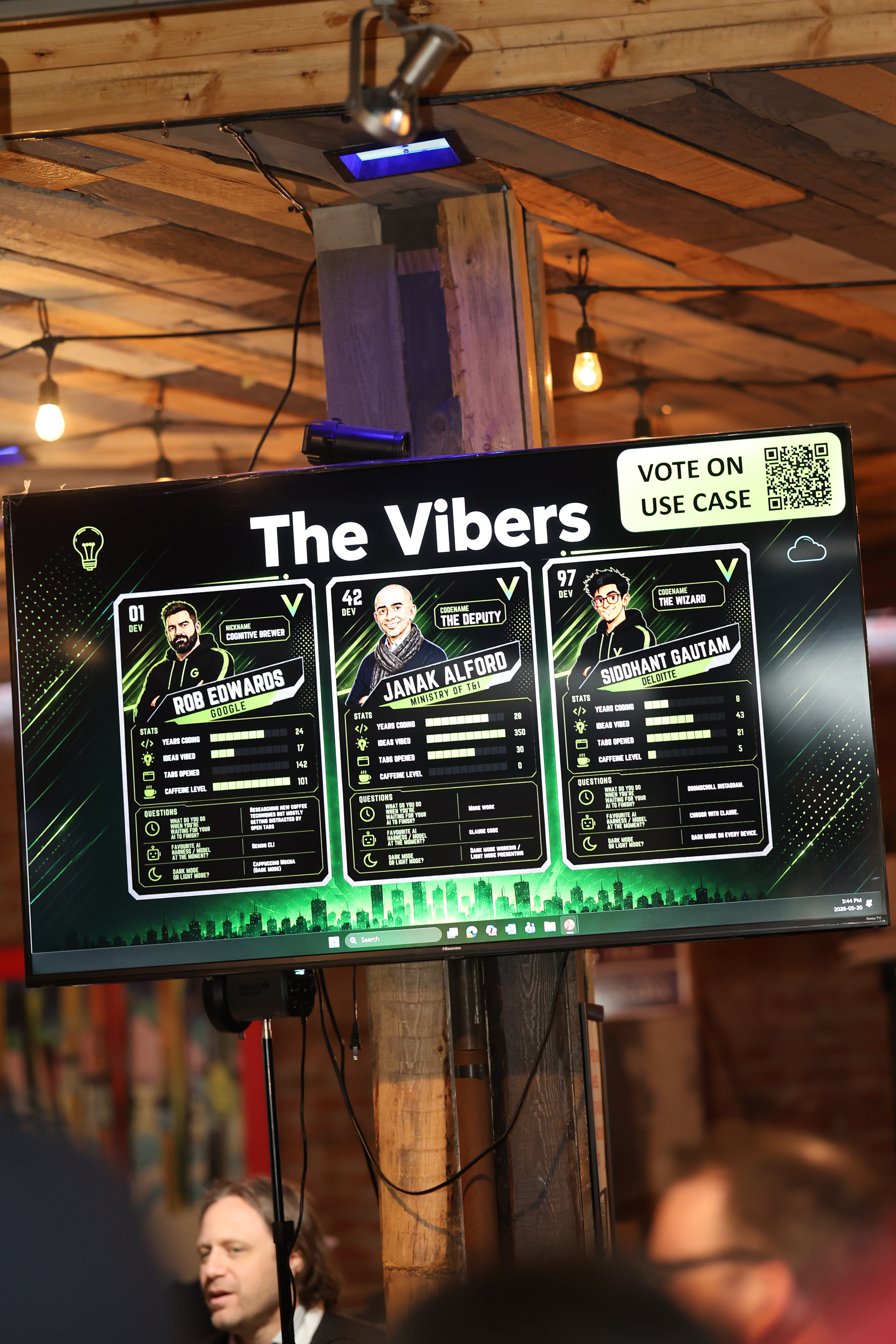 A large presentation screen showing &lsquo;The Vibers&rsquo; coder profile cards for Dev 01 Rob Edwards, Dev 42 Janak Alford, and Dev 97 Siddhant Gautam, displaying coding stats and questions