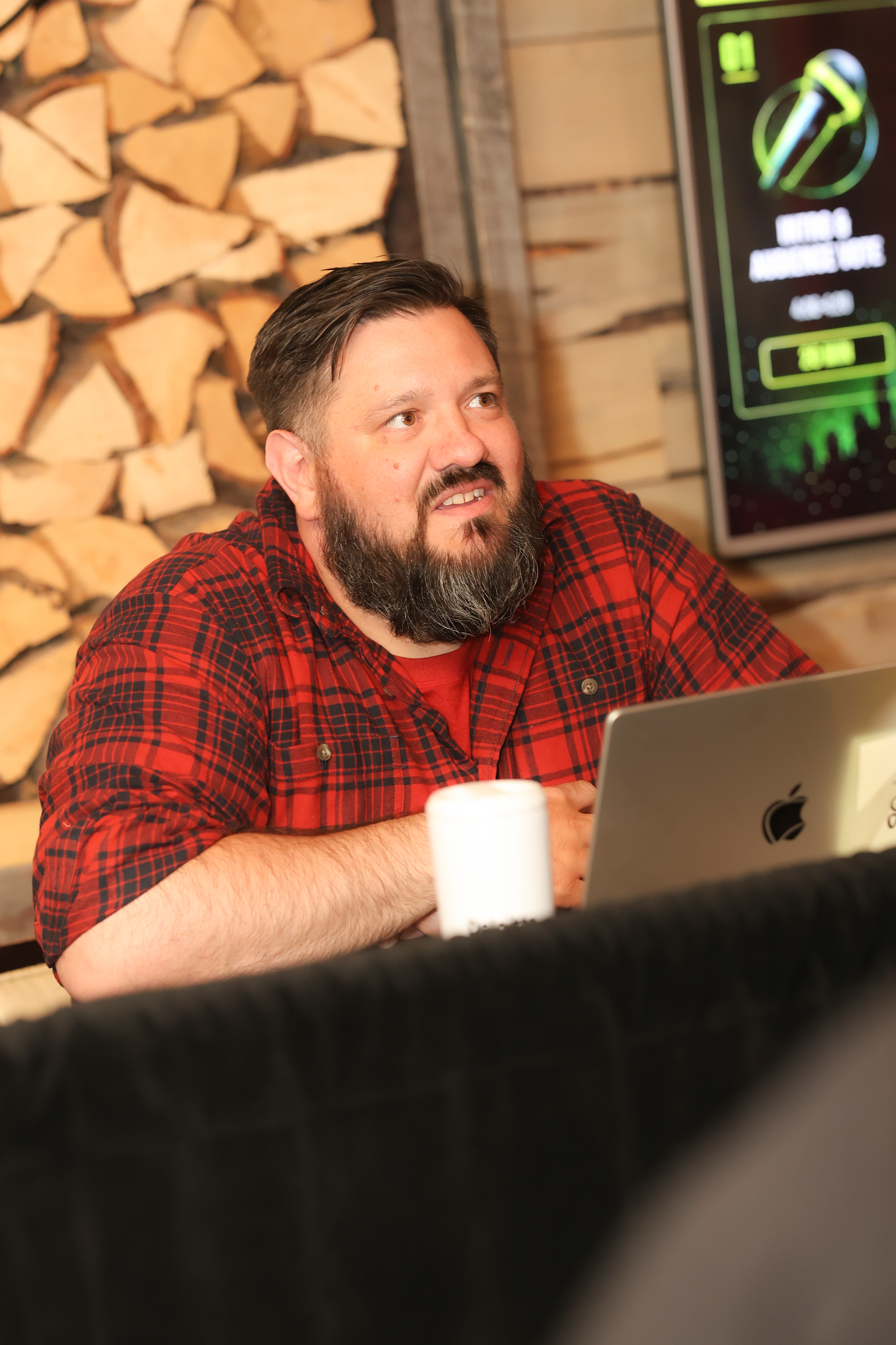 Coder Rob Edwards sitting at his workspace, smiling warmly, with his open laptop and a white coffee mug resting on the table in front of a rustic wooden background