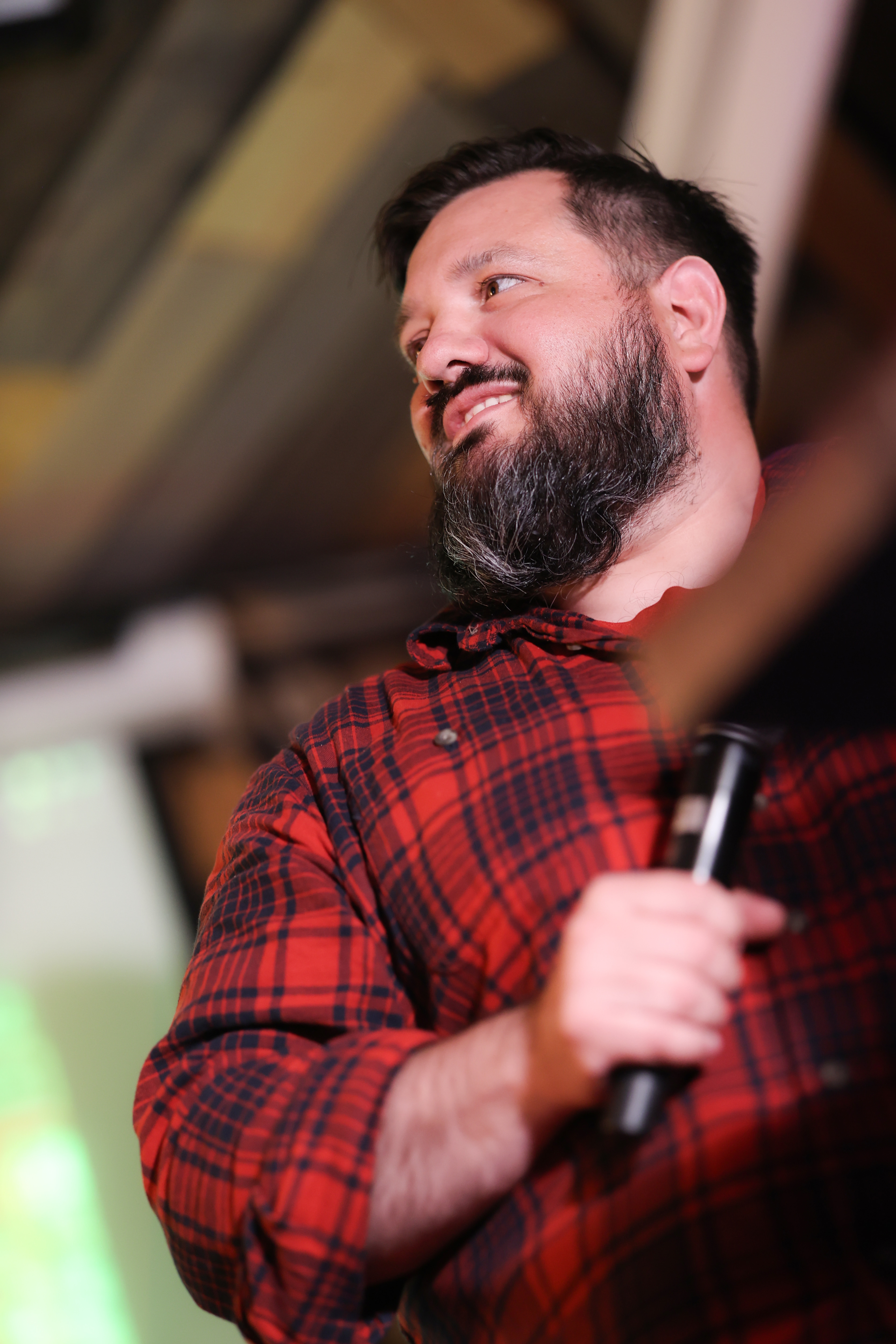 Rob Edwards standing on stage, smiling and speaking into a handheld microphone under the stage lighting, engaging the audience