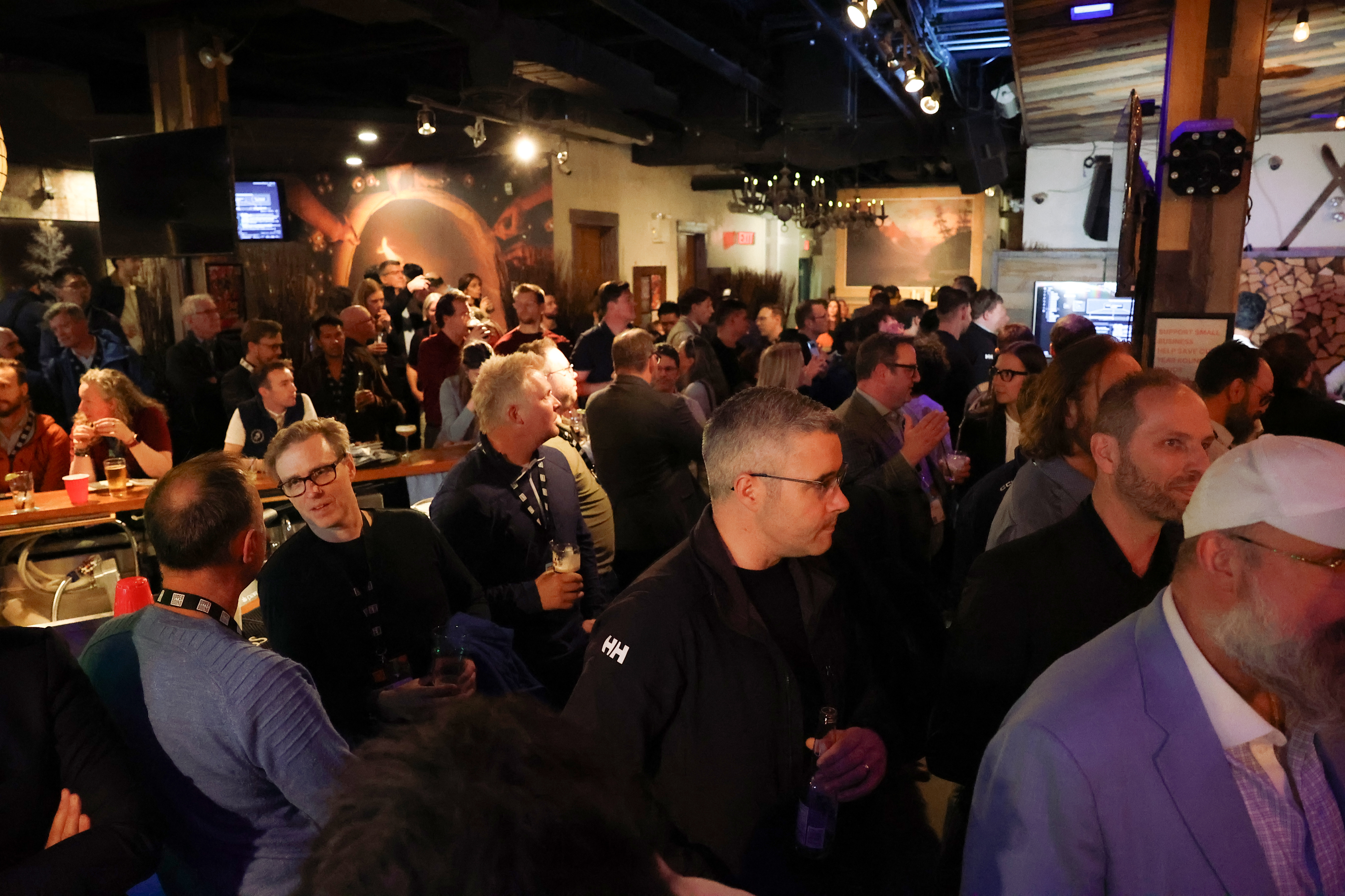 A wide-angle view of the packed, energetic bar at Rocky Mountain Ice House during Upper Bound 2026, with over 200 attendees standing and socializing under warm lighting