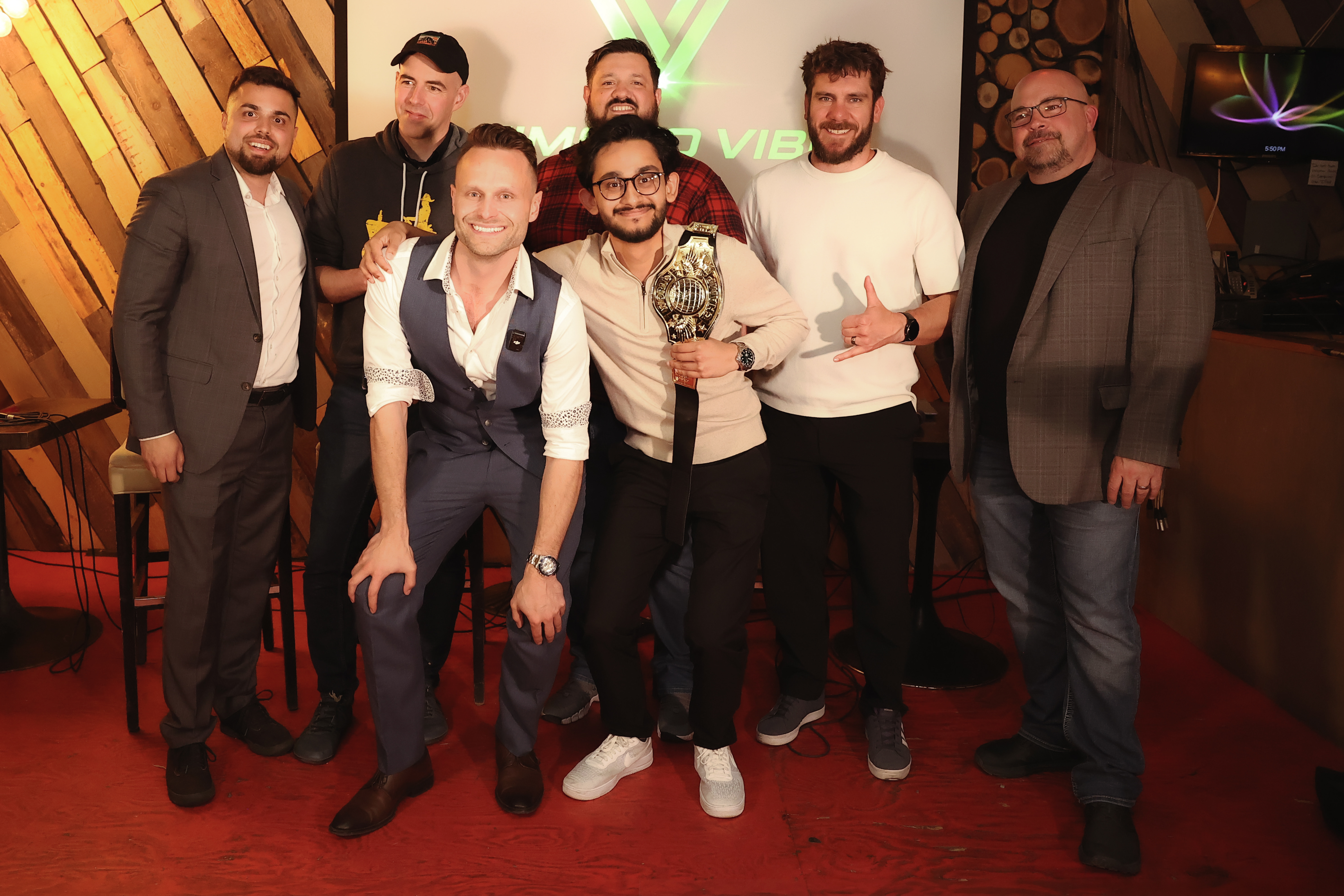 A celebratory group photo on stage showing Siddhant Gautam proudly holding the heavy gold Vibe Games championship belt, flanked by Rob Edwards, Janak Alford, and the event judges